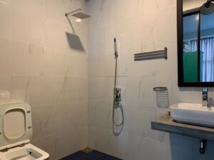 A modern bathroom with white tiles, shower, toilet, concrete sink, white basin, and black-framed mirror.